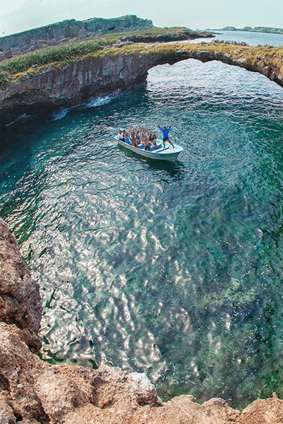 Group of people in a boat inside Marietas with natural bridge behind them