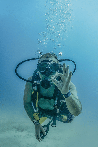 Male scuba diver singling to camera