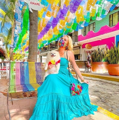 Young blond woman in turquiose dress sitting on a bench on a colorful street in Sayulita Mexico